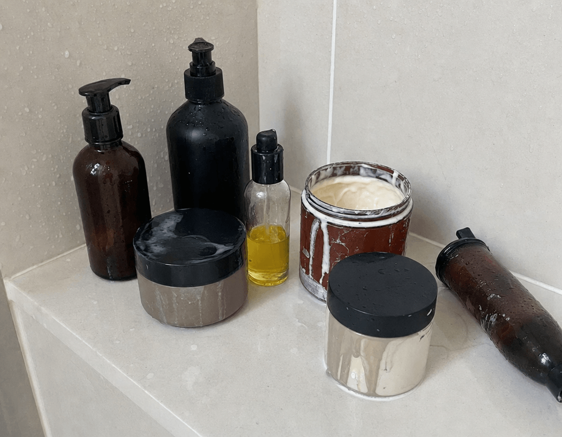 Foto real: repisa de ducha con 5-6 botes de mascarillas y aceites usados («lo he probado todo»)